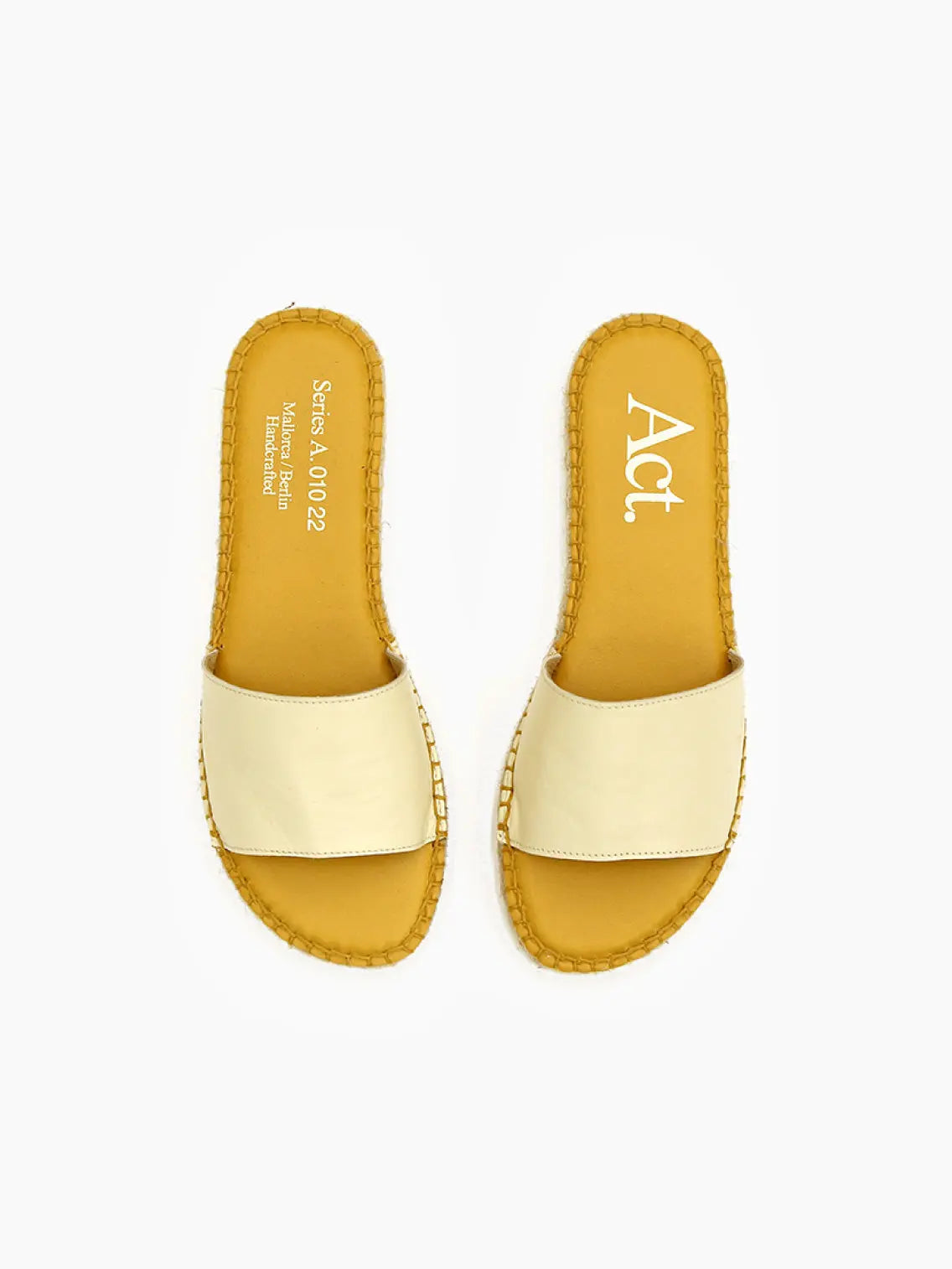 A pair of Ennart White Espadrilles from Act Series, available at Bassalstore in Barcelona, lie on a white background. The insoles have text on them, including the word "Act." The edges of the soles have a woven texture, resembling straw or wicker.