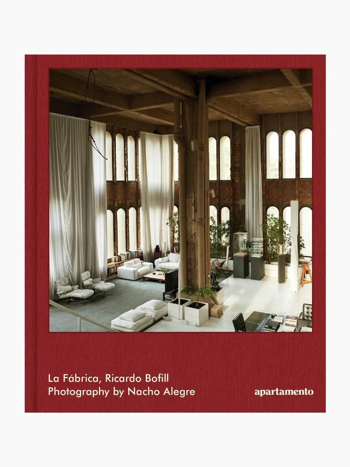 Interior view of La Fábrica, Ricardo Bofill, showing a spacious, high-ceilinged room with large arched windows, white sofas, and tall indoor plants. Exposed brick walls and wooden beams add to the rustic yet modern aesthetic of this Barcelona gem. Text at the bottom credits Ricardo Bofill and Nacho Alegre. Brand name: Apartamento