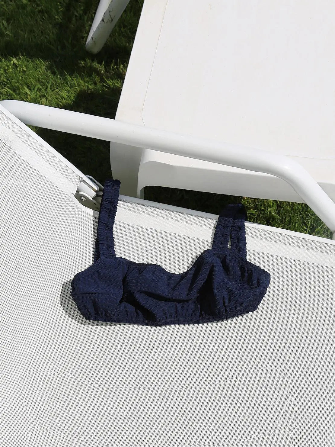 A Marine Bikini Top - Bassal from Bassal is placed on a white lounge chair outside on a sunny day. The lounge chair is positioned on green grass, perfect for soaking up the Barcelona sun.