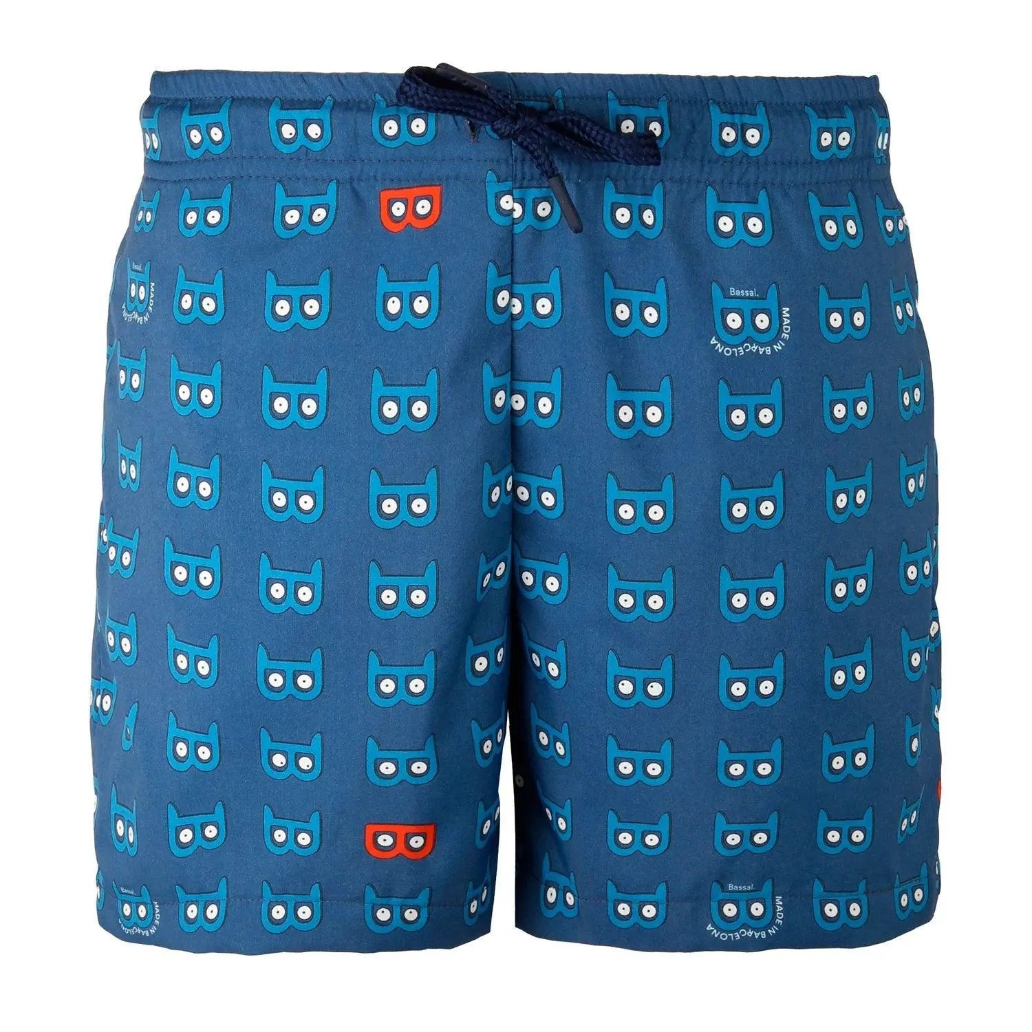 A pair of blue Mask Kids Swimwear with a cute owl pattern, neatly folded in an orange-bordered white box. A tag with the brand name "Bassal" and a plastic zipper bag are visible. The brand's name "Bassalstore" is printed on the box, showcasing its Barcelona roots.