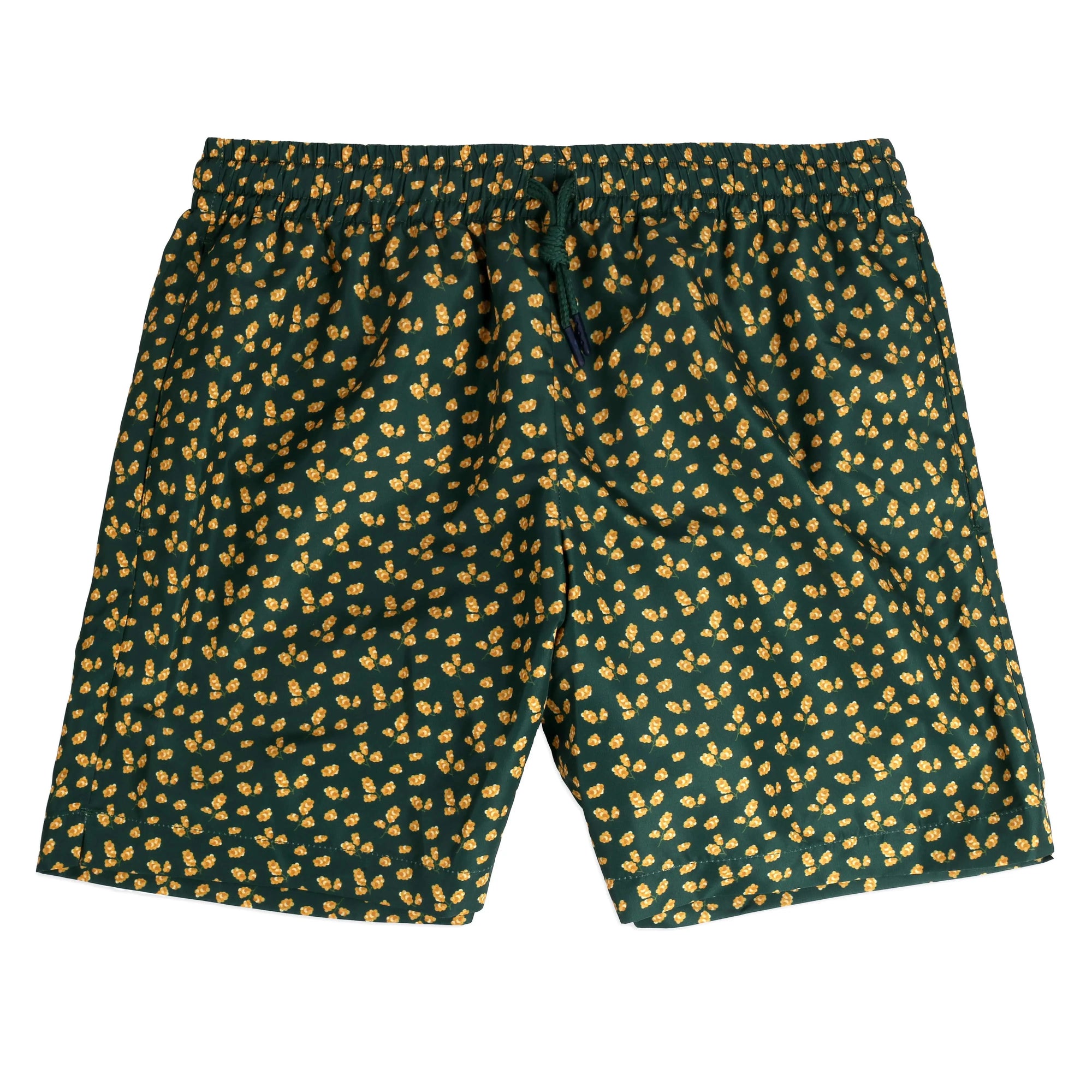 An open white box labeled "Bassal" reveals neatly folded dark green Mimosa Swimwear adorned with a yellow floral pattern. A smaller card with text lies on the swimwear, along with a small zipped bag containing a blue item. Discover this and more unique pieces at bassalstore, your go-to shop in Barcelona.