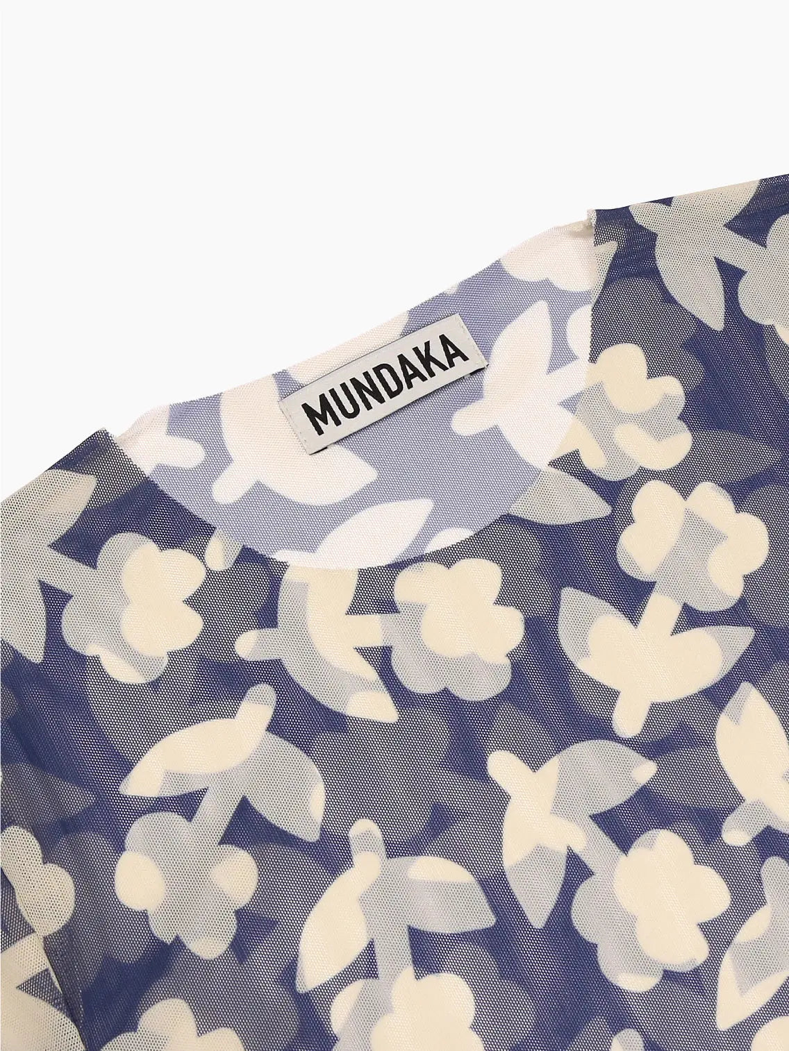 A Recycled Tulle T-Shirt Blue with a blue and white floral pattern. The flowers are abstract in design, and the shirt's fabric appears lightweight and semi-transparent. Perfect for a breezy day in Barcelona, this stylish piece from Mundaka is now available at Bassalstore.