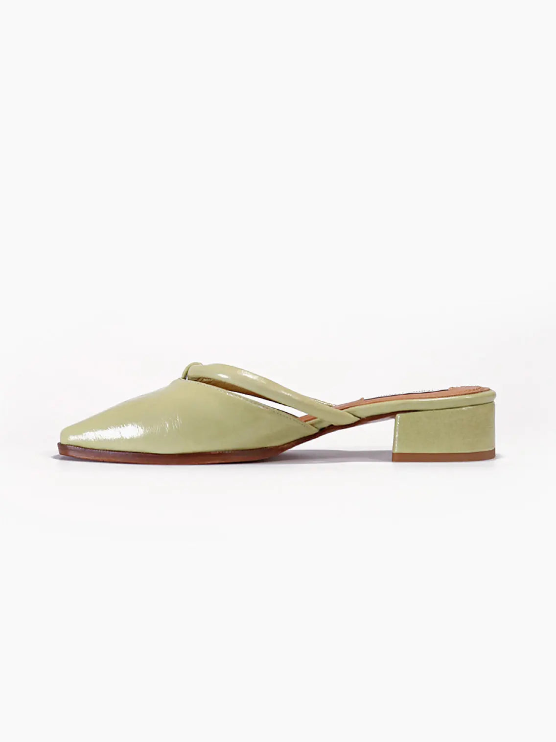 Side view of a light green patent leather Simone Oil Sandals by About Arianne with a pointed toe, a low block heel, and a twisted strap detail across the front. The sole is a contrasting brown color. Photographed on a white background, this stylish piece is available at Bassalstore in Barcelona.