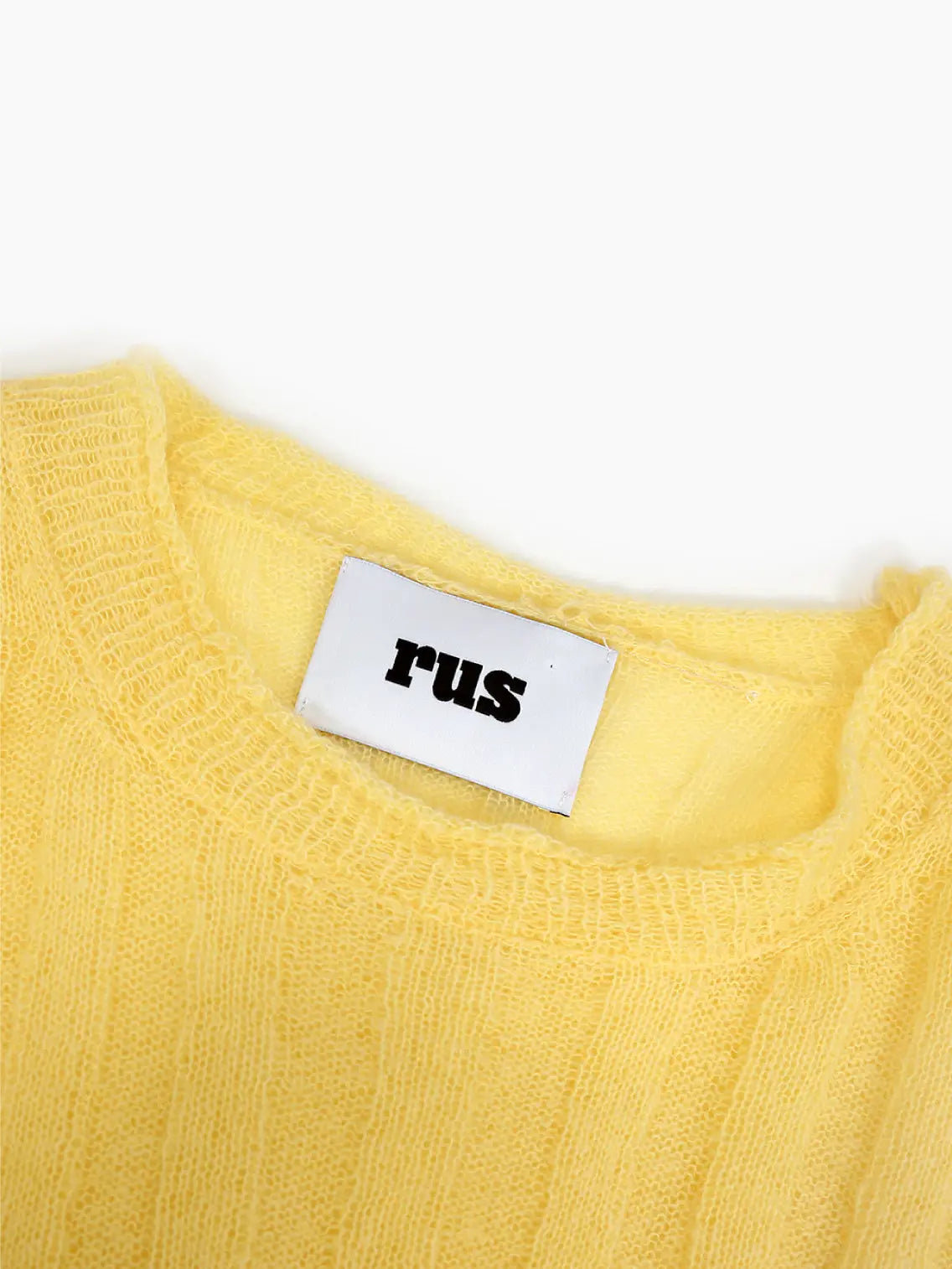 A yellow long-sleeve sweater with a ribbed texture is laid flat on a white background. It has a round neckline and a simple, relaxed fit. The inner label at the neckline reads "Rus." Available now at Bassalstore in Barcelona.