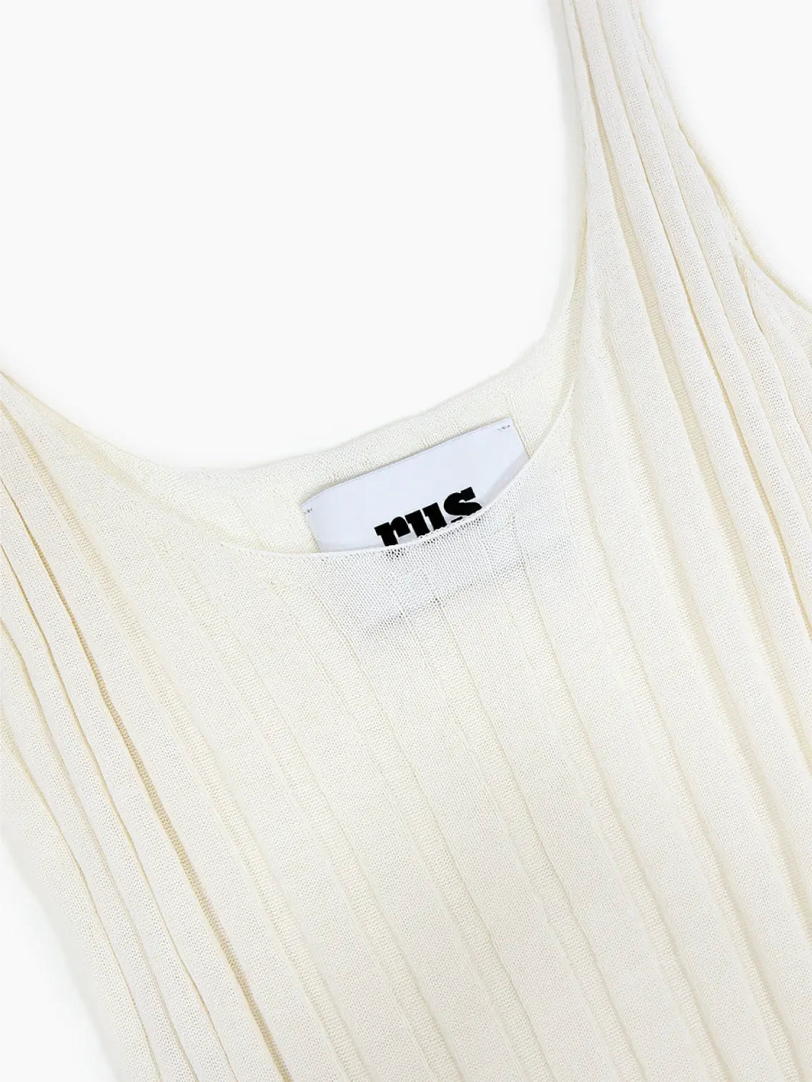 A Stella Top Chalk by Rus, sleeveless, cream-colored, ribbed knit dress with thin straps and a scoop neckline, laid flat on a white background. The dress has a fitted, slightly flared silhouette and features a small white label with black text on the inside of the back neckline. Available exclusively at Bassalstore in Barcelona.