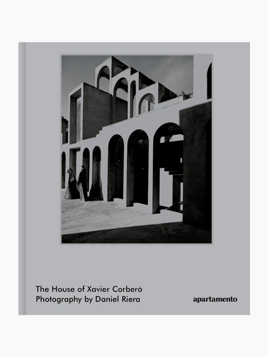 Cover of the book "The House of Xavier Corberó" by Apartamento with photography by Daniel Riera, published by Apartamento. The cover features a black and white photo of a building with arches and shadows in Barcelona. A person stands near one of the arches in the background. Available at bassalstore.