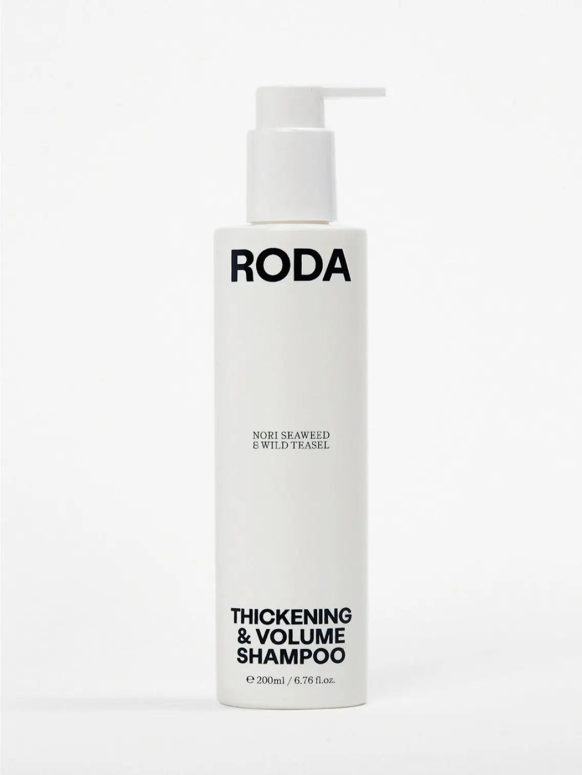 A bottle of Roda Thickening & Volume Shampoo is placed alongside its gray box. The shampoo bottle is white with a pump dispenser and black text. Nearby, there is a sprig of dried flowers and a small pile of dark seaweed. Available at Bassalstore in Barcelona, the bottle contains 200ml (6.7 fl. oz.).