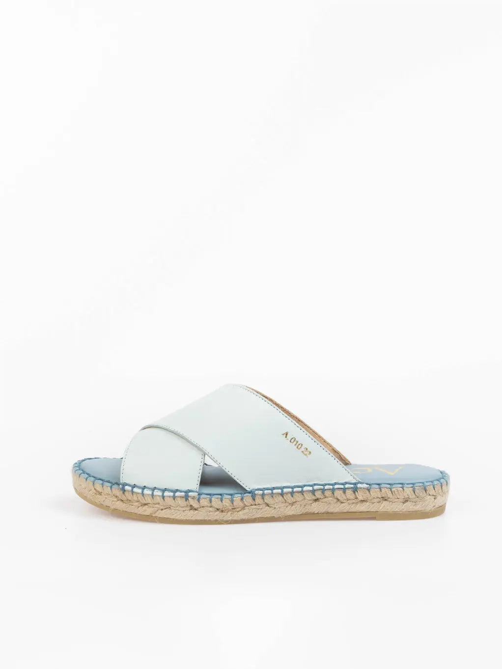A pair of Uccle Light Blue Espadrilles with crisscross straps and exposed toes. The insole features gold text on the left sandal, and the stitching around the edges is in a matching light blue color. The espadrilles from Act Series are placed on a white background.