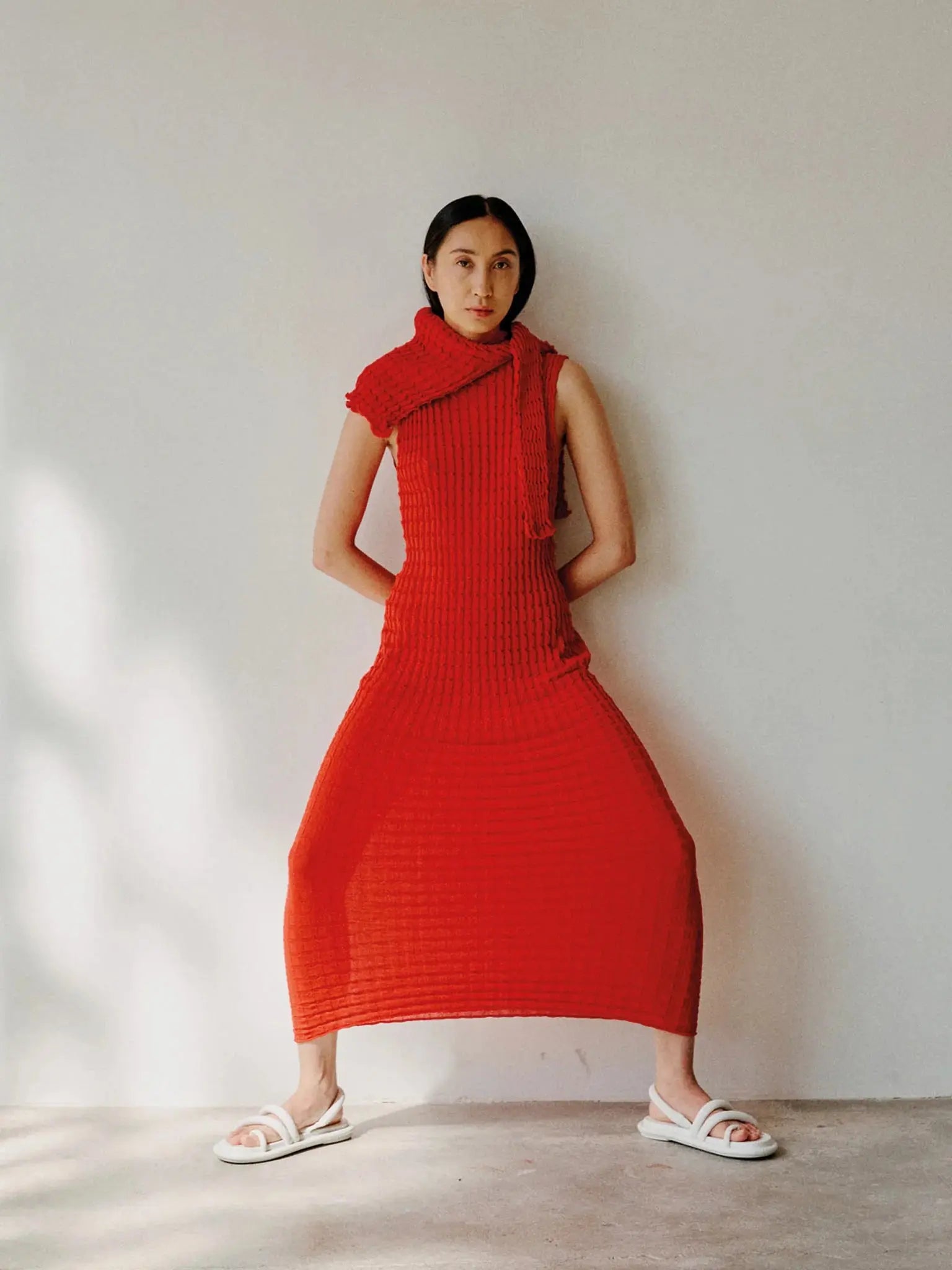 A sleeveless, full-length red dress with a high neckline. The Udon Dress Red by Rus features a textured, ribbed pattern throughout and has a fitted silhouette. The hemline is slightly scalloped, giving a subtle decorative edge to the garment. Find it at Bassalstore in Barcelona for an elegant touch to your wardrobe.