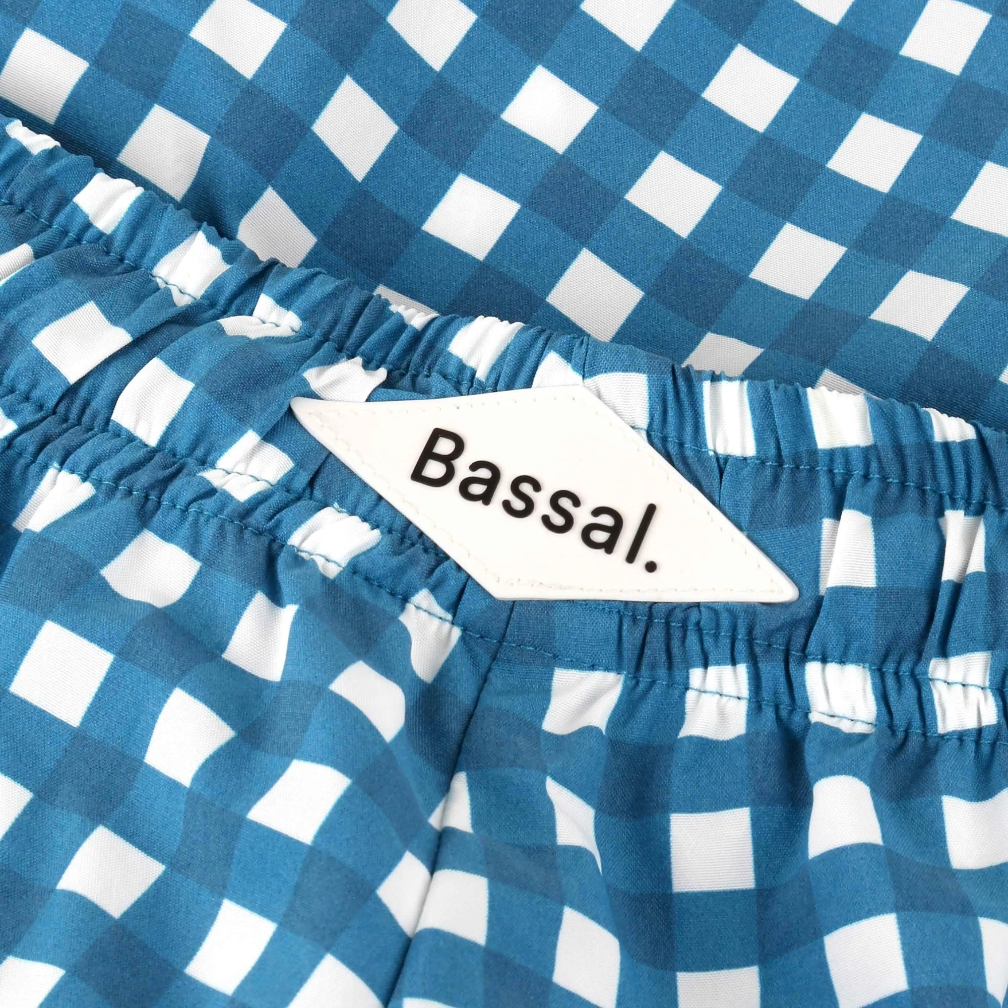 A white box from bassalstore contains Vichy Swimwear, neatly folded, and accompanied by a tag displaying the brand name "Bassal." The box lid is partially open and also has "Bassal" written on it. A touch of Barcelona style right at your doorstep.